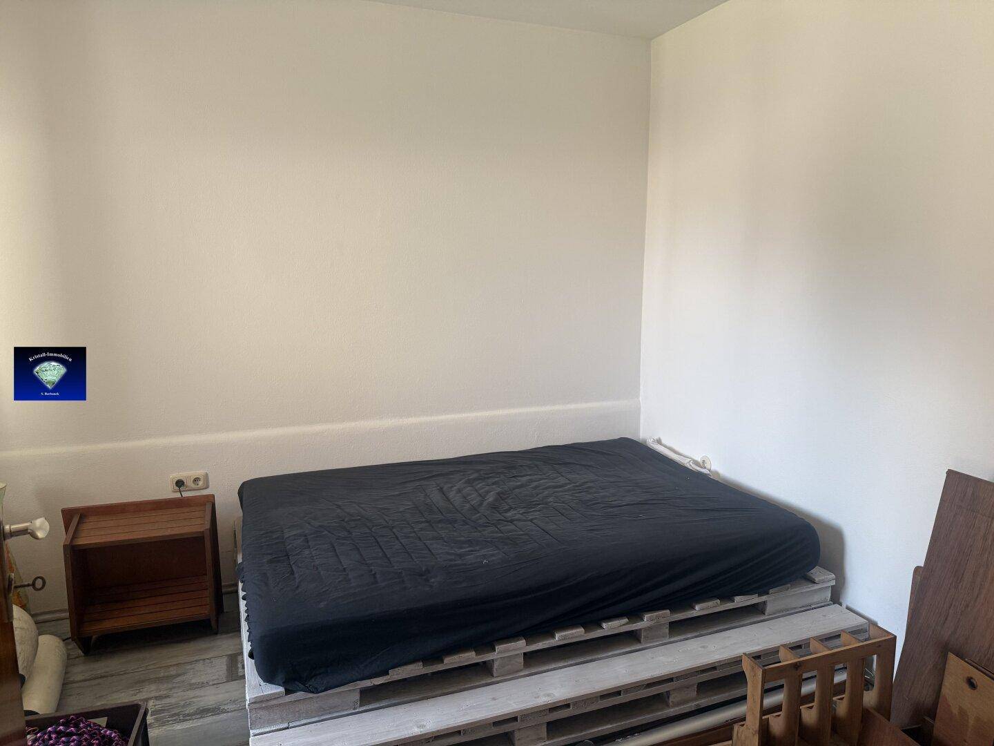 Schlafzimmer mit einem Bett auf Palettenbasis und einem Nachttisch, bereit für individuelle Gestaltung.