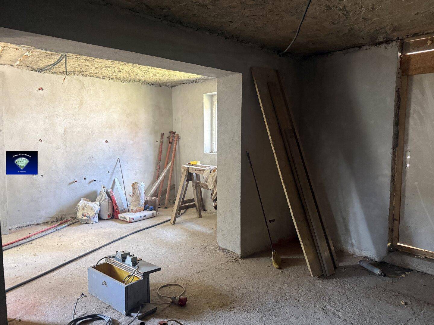 Raum im Rohbauzustand mit sichtbaren Leitungen und Baumaterialien, bereit für den Ausbau.