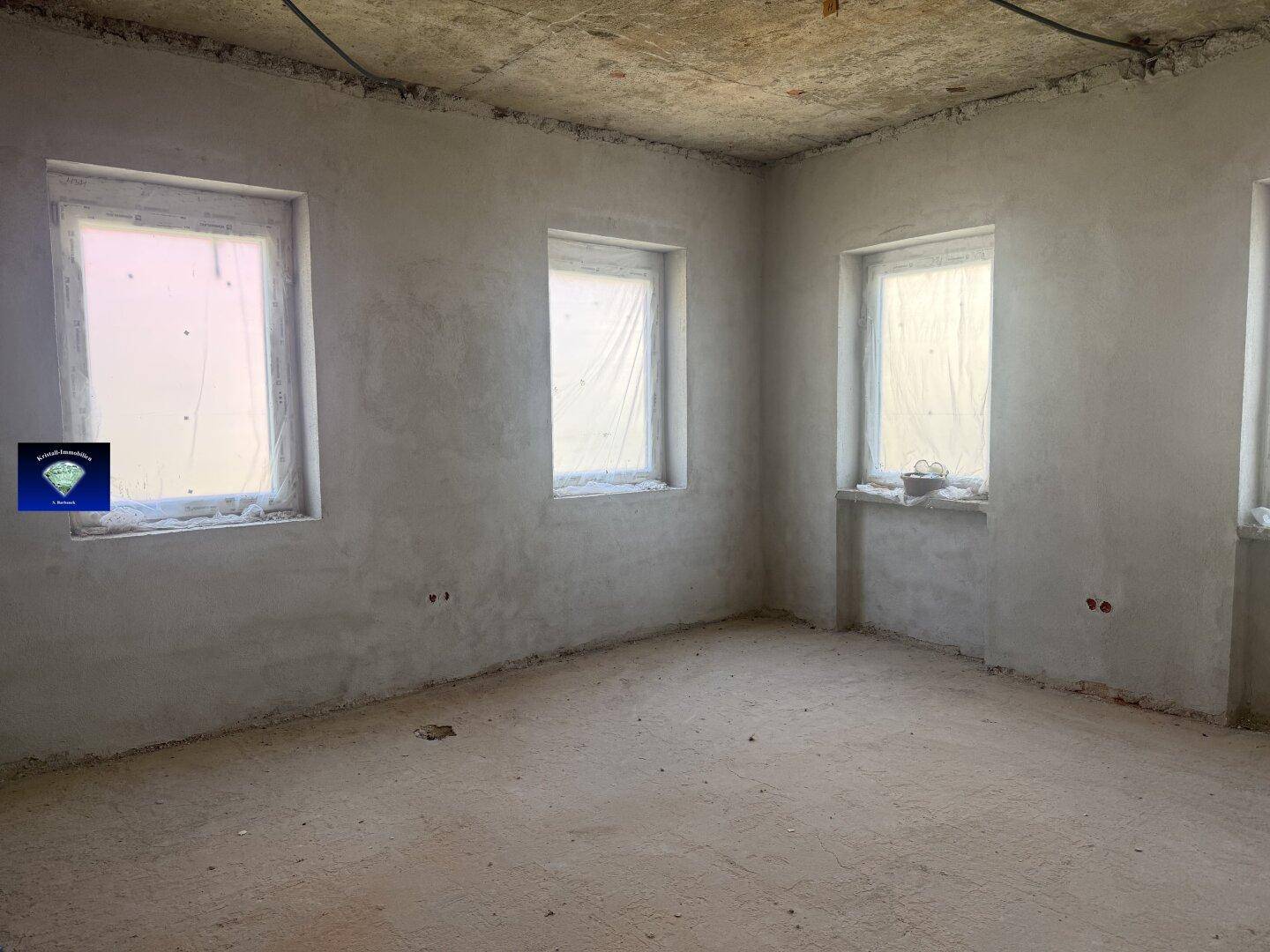 Unfertiger Raum mit mehreren Fenstern und rohen Wänden, wartet auf den Innenausbau.