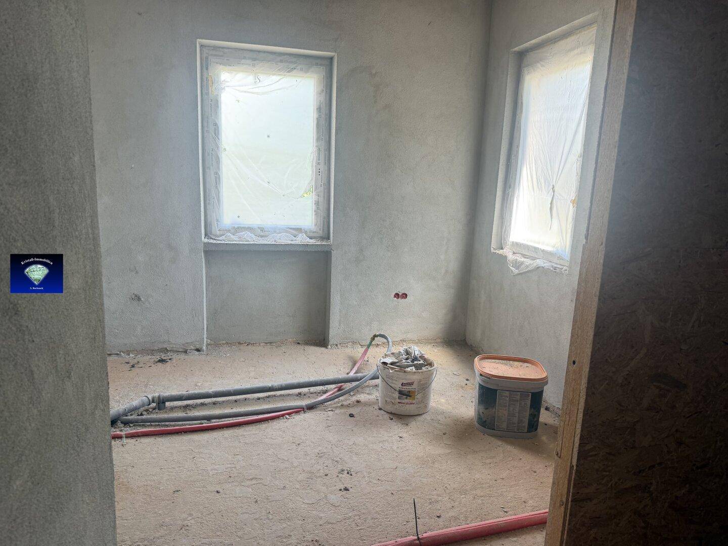 Raum im Rohbau mit Fenstern und sichtbaren Installationen, bereit für die Fertigstellung.