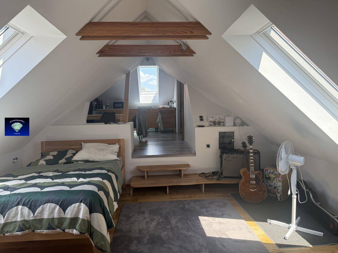 Helles Dachgeschoss-Schlafzimmer mit schrägen Wänden, Dachfenstern und einem offenen Wohnbereich.