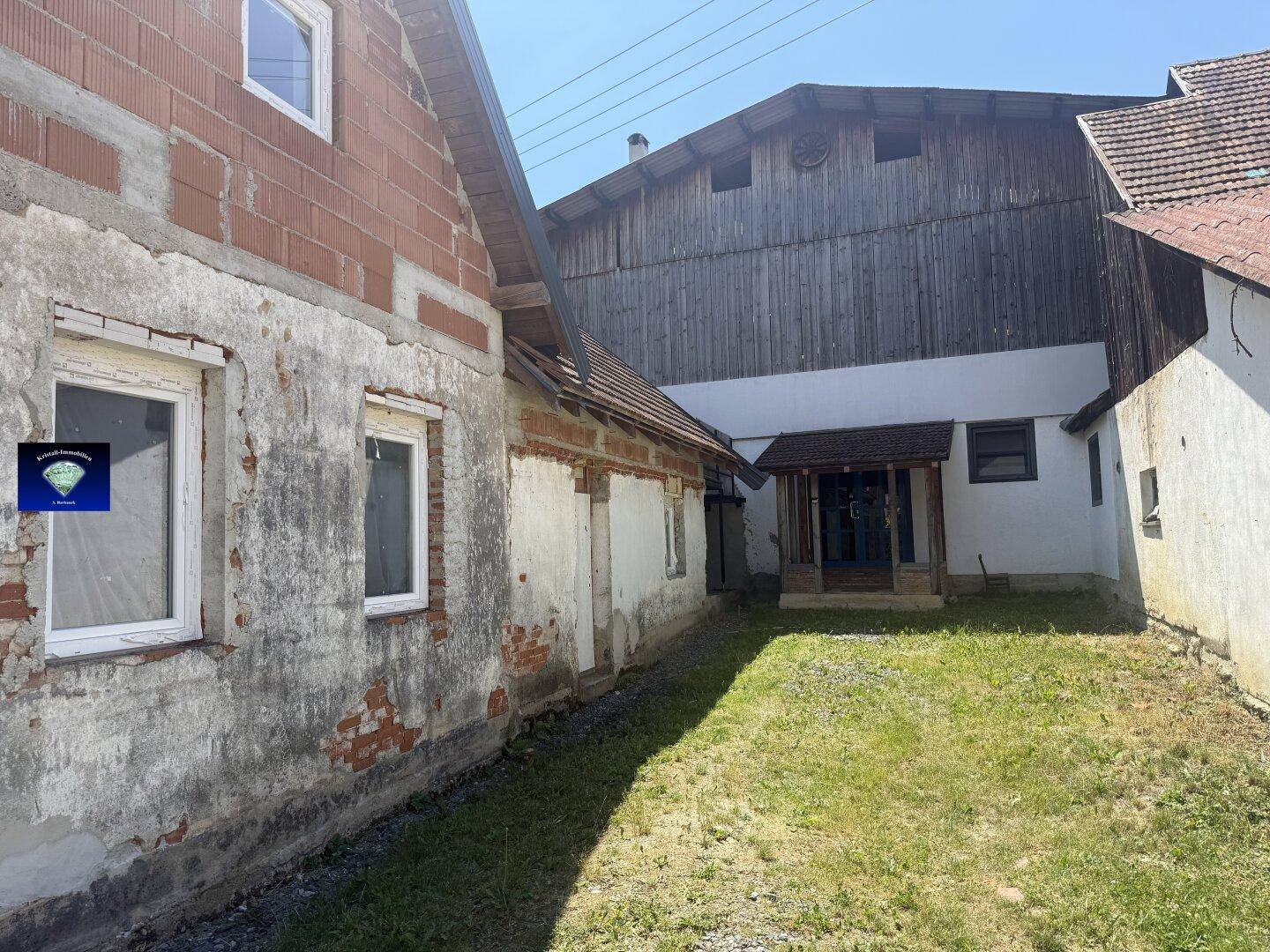 Ländliches Anwesen mit einem alten Gebäude, einem Gartenbereich und einem angrenzenden Holzschuppen.