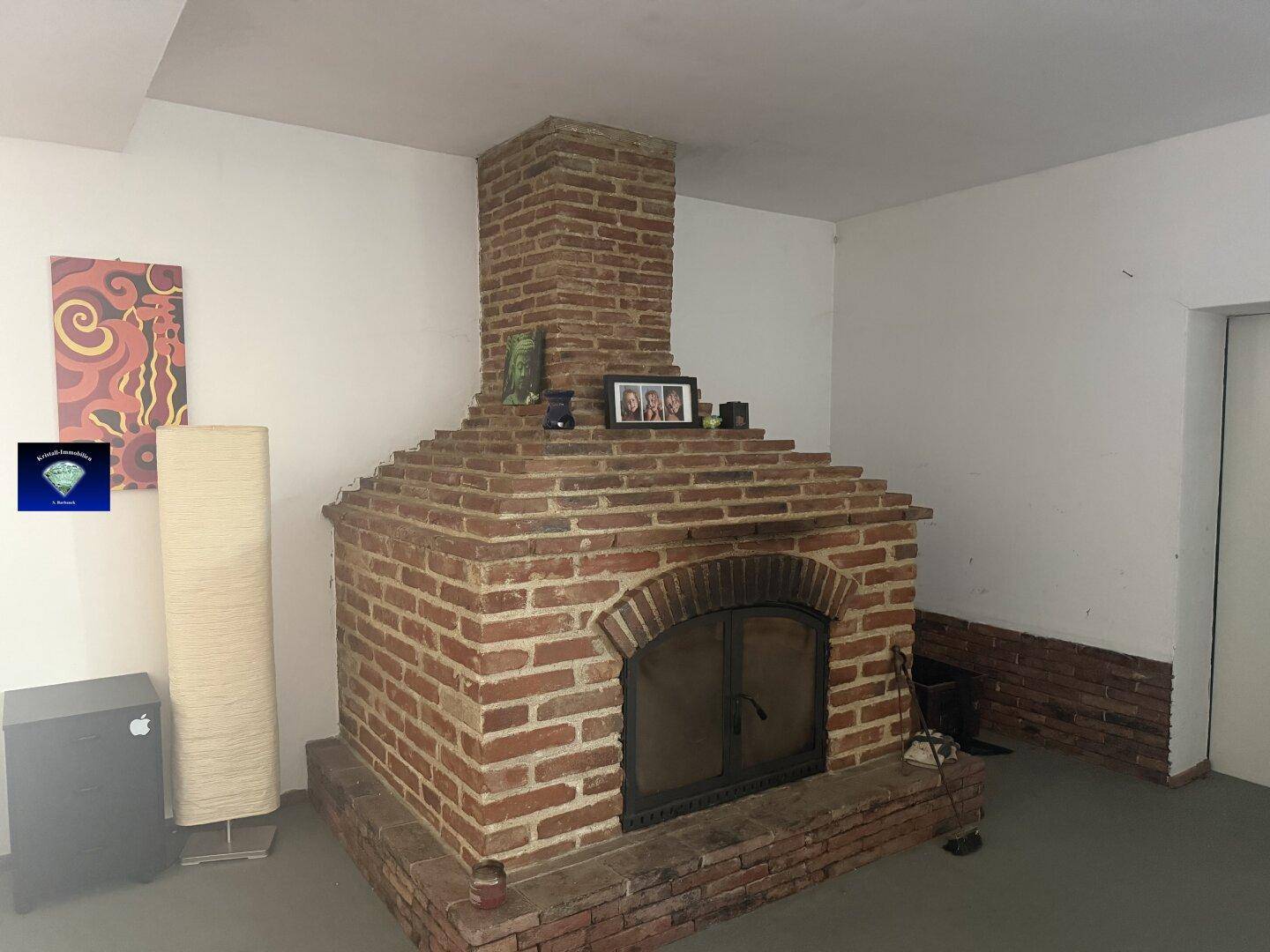 Geräumiges Wohnzimmer mit einem großen gemauerten Kamin als Mittelpunkt und schlichter Einrichtung.