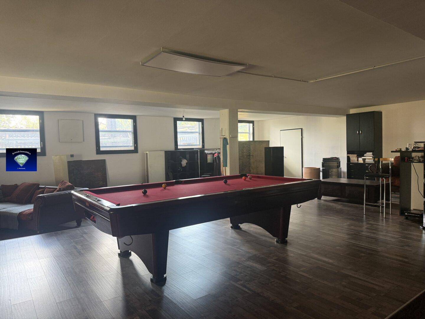 Großer Spielraum mit Billardtisch, Sofa und Fenstern, die viel Tageslicht hereinlassen.