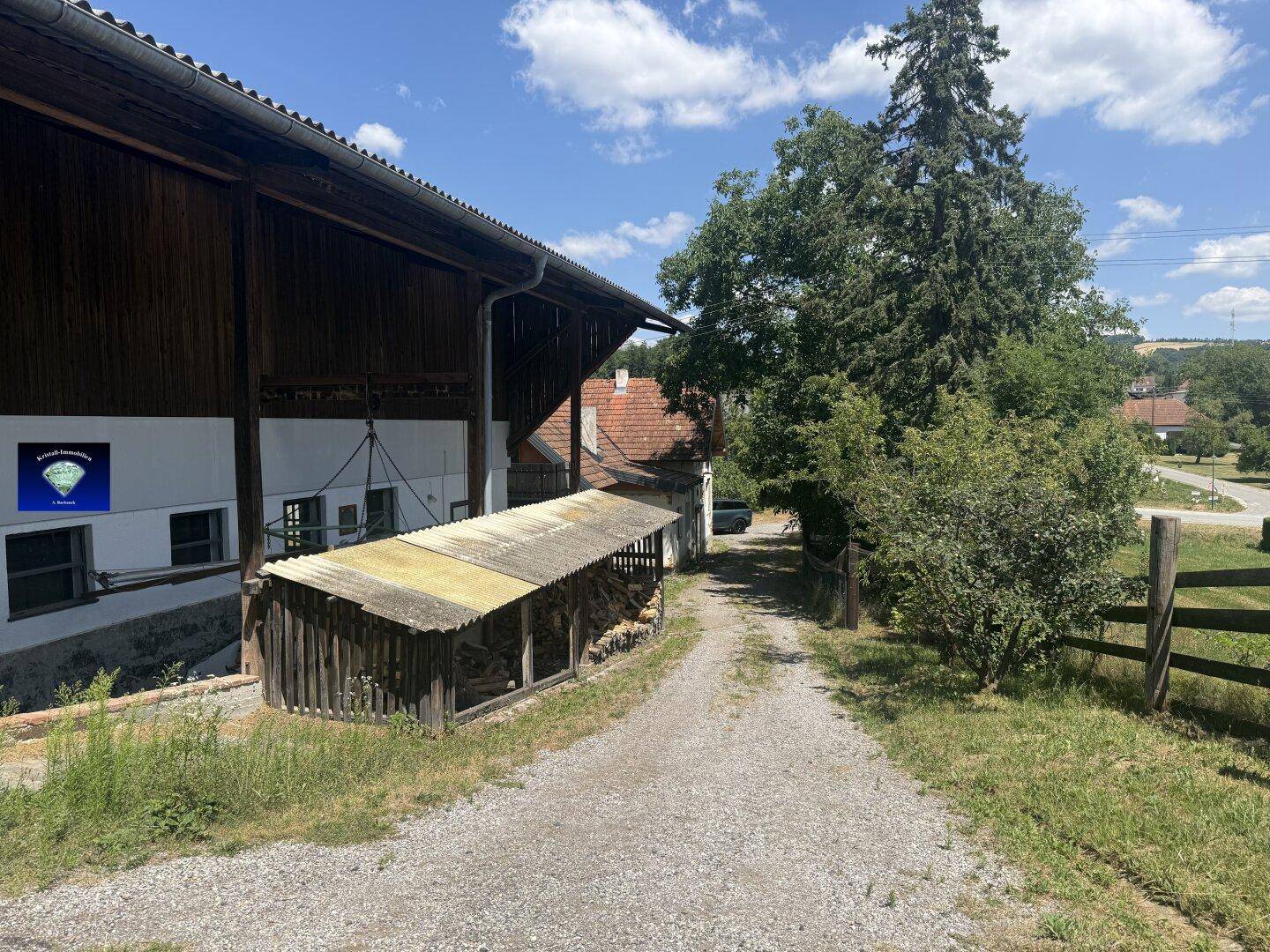 Ländliches Anwesen mit Zufahrt, Holzschuppen und viel Grün, umgeben von Natur.