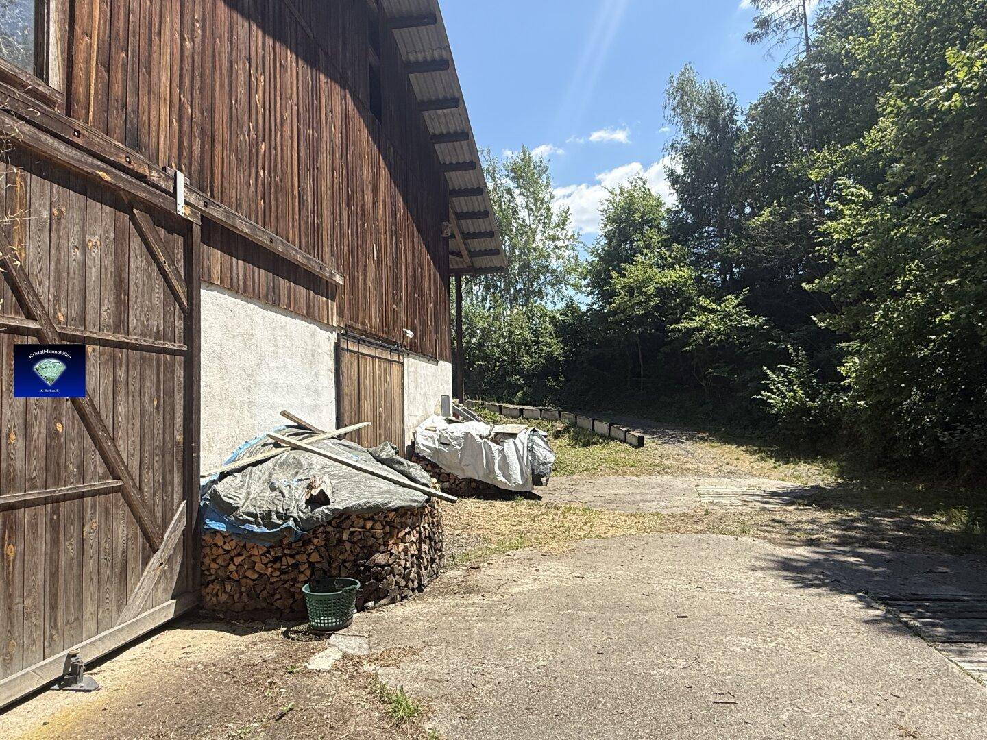 Rustikales Holzgebäude mit gestapeltem Brennholz und einem befestigten Weg im Grünen.