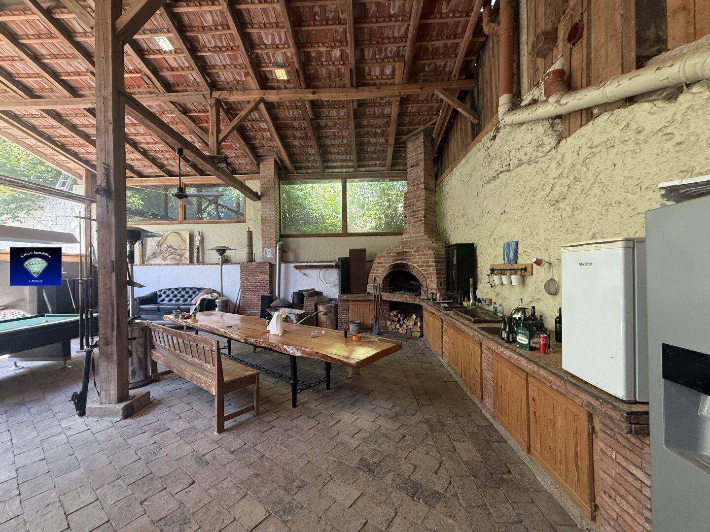 Rustikale Wohnküche mit großem Holztisch, gemauertem Ofen, Arbeitsplatte und freiliegenden Holzbalken.