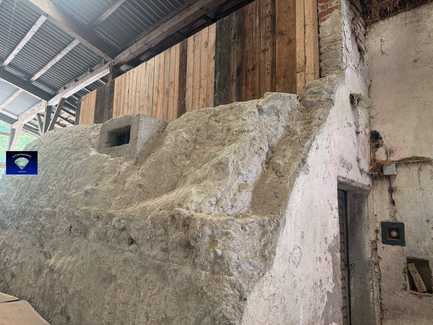 Innenansicht eines Scheunengebäudes mit massiver Betonstruktur und Holzwänden unter dem Dach.
