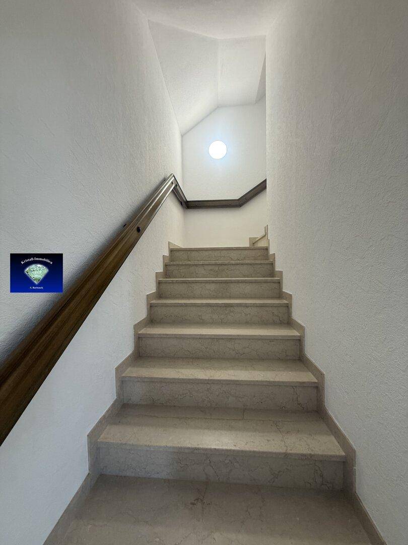 Marmortreppe mit Holzgeländer führt in die oberen Stockwerke, gut beleuchtet.