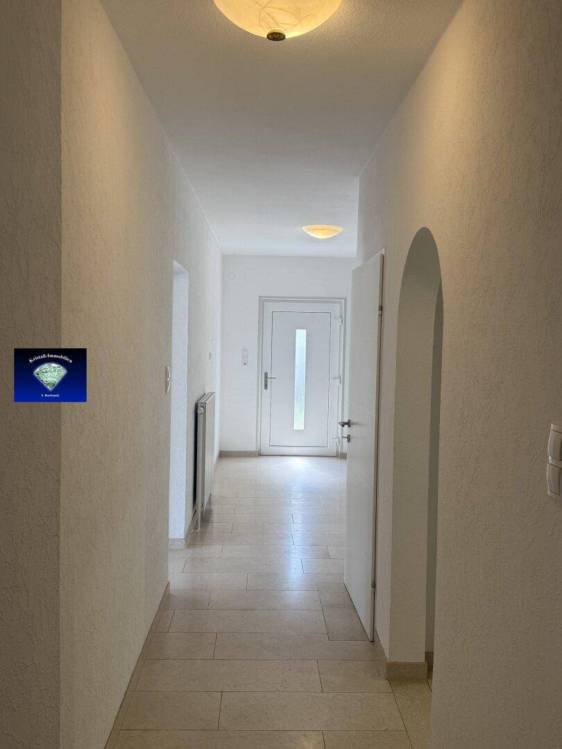 Heller Flur mit Fliesenboden und weiß gestrichenen Wänden, führt zum Eingangsbereich.