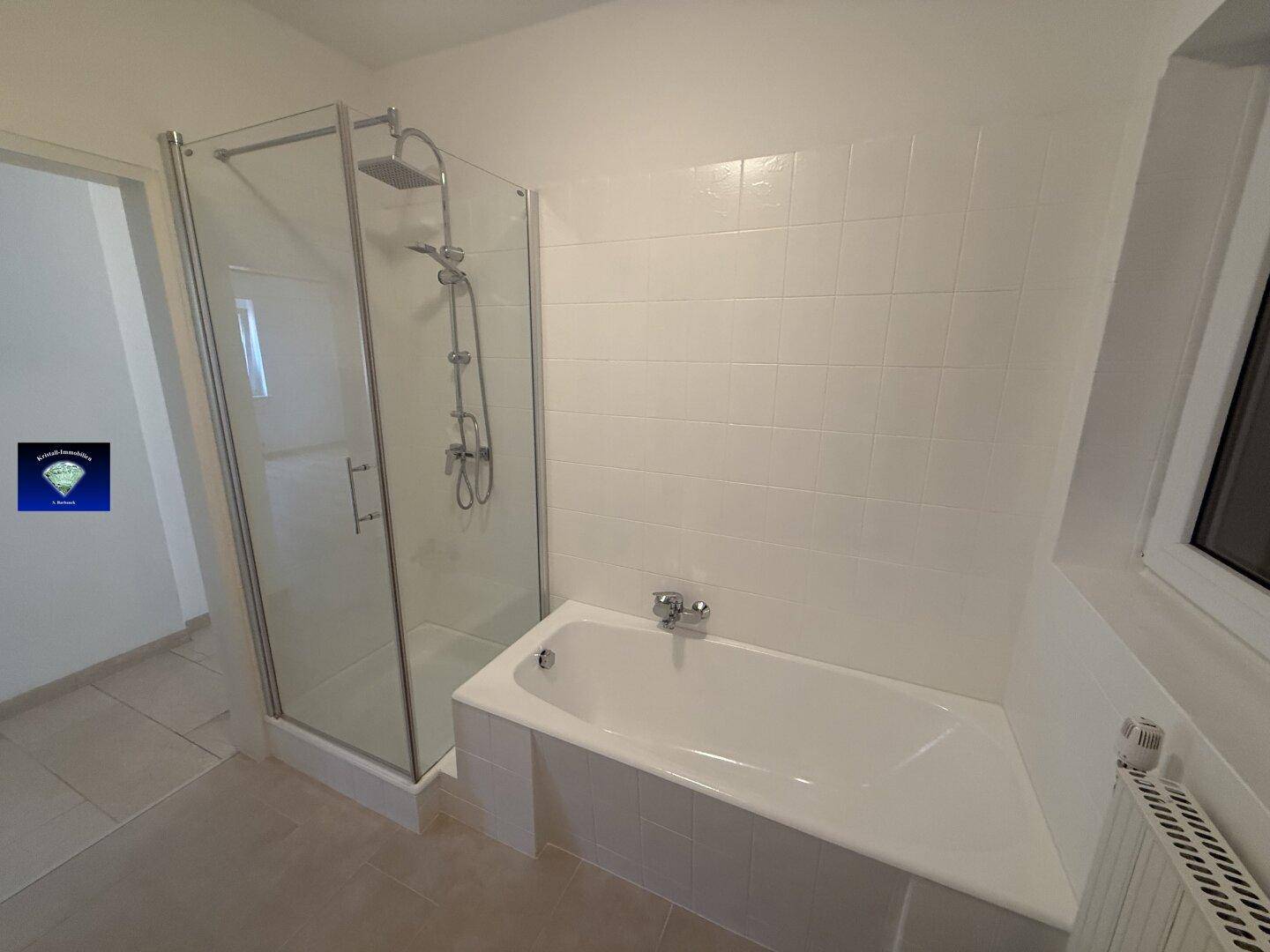 Badezimmer mit Badewanne und Duschkabine, weißen Fliesen und Fenster für Tageslicht.