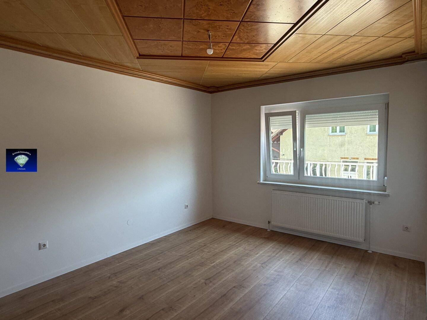 Zimmer mit Holzdeckenpaneelen und Laminatboden, bietet Blick auf den Balkon.