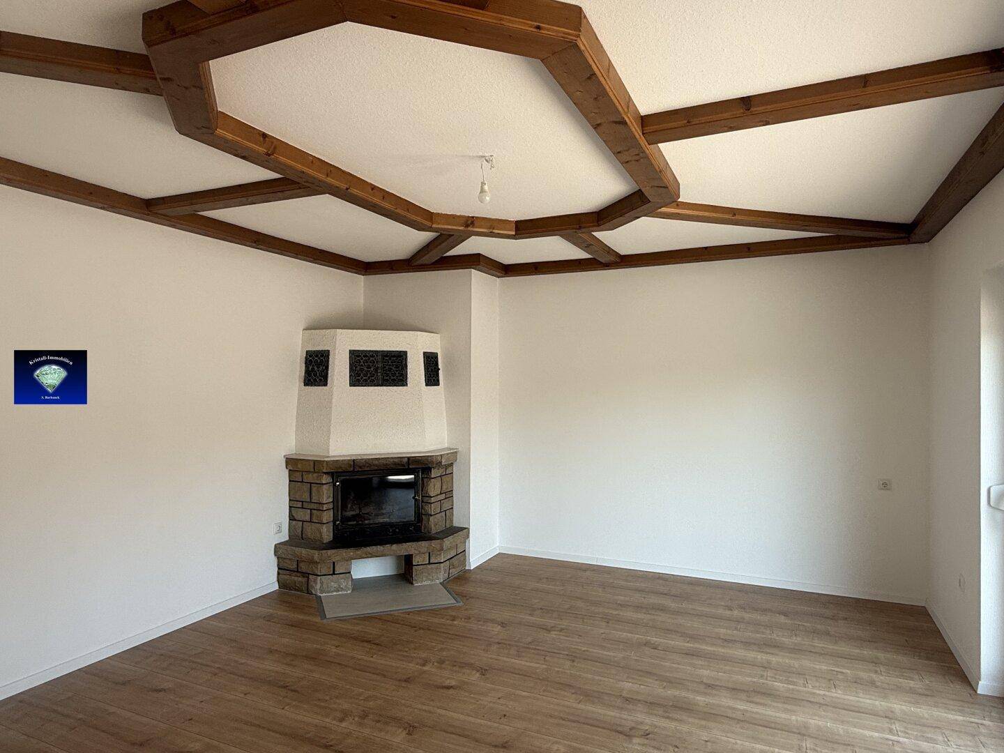Wohnzimmer mit Holzbalkendecke, Kamin und Laminatboden, bereit zur individuellen Gestaltung.