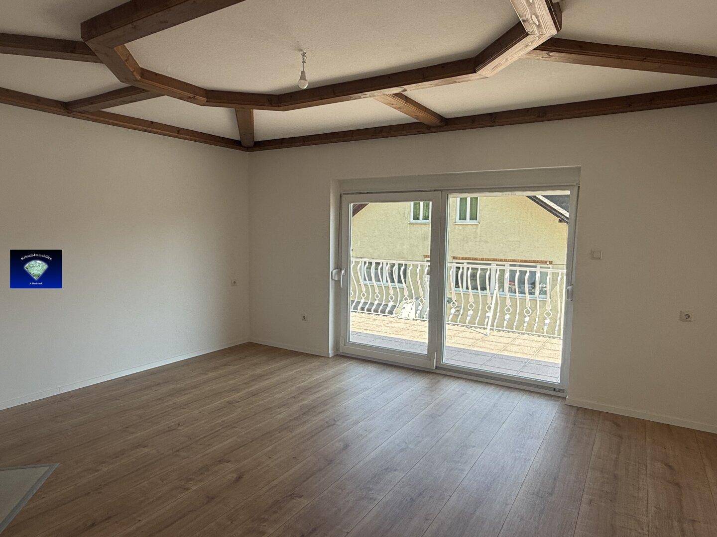 Helles Wohnzimmer mit Balkonzugang durch große Schiebetüren und Laminatboden.