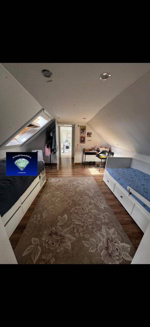 Helles Dachzimmer mit schrägen Wänden, Dachfenster, Bett und Schreibtisch.