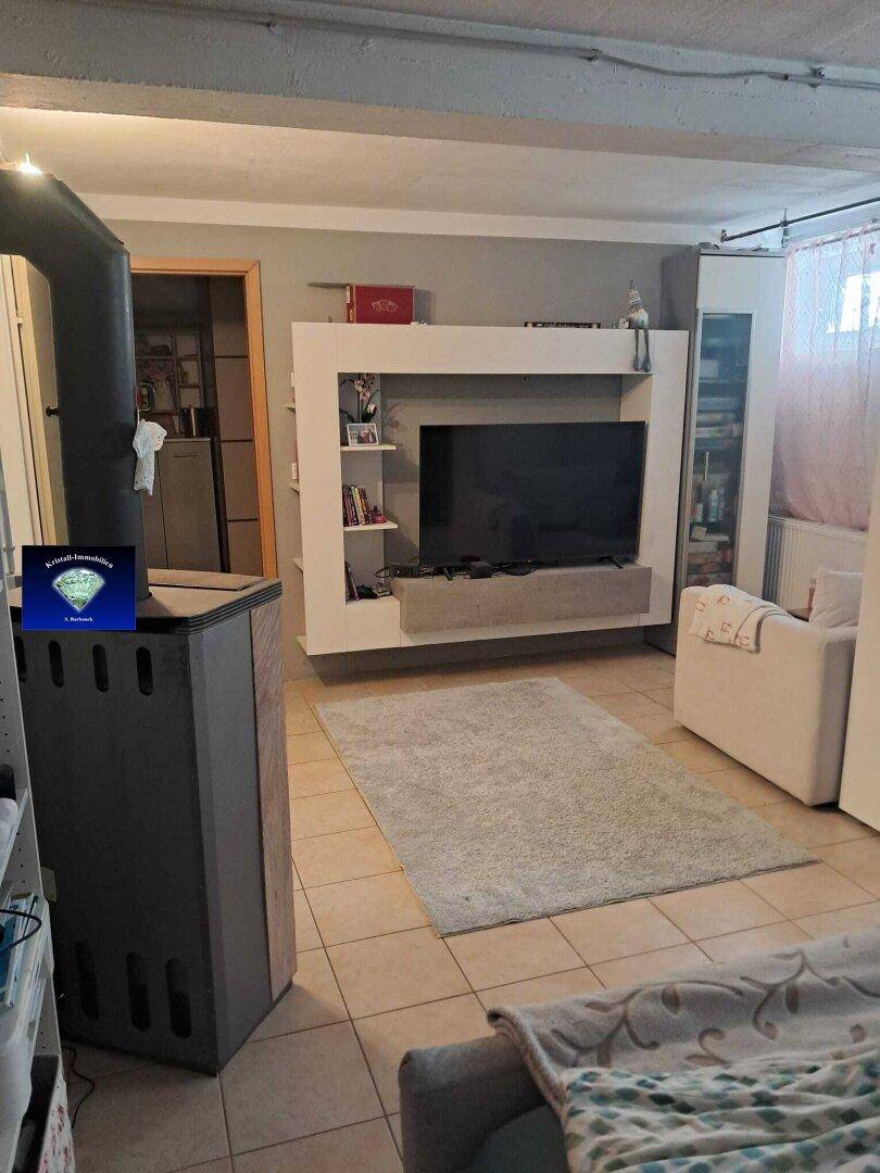 Ausgebauter Kellerraum mit Fliesenboden, Fernseher und Holzofen.