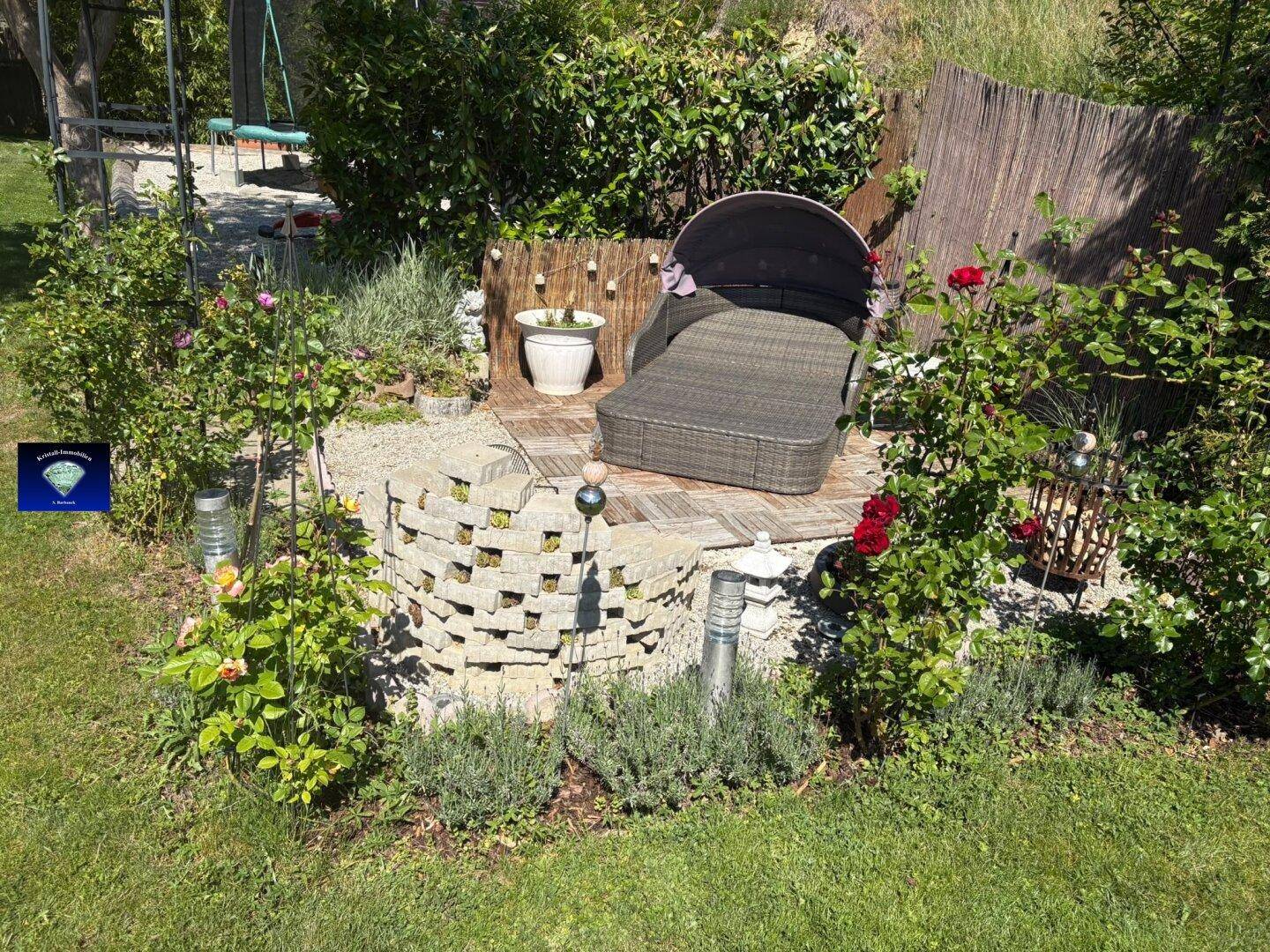 Dekorativer Gartenbereich mit Blumen, Rasen und einer Sonnenliege.