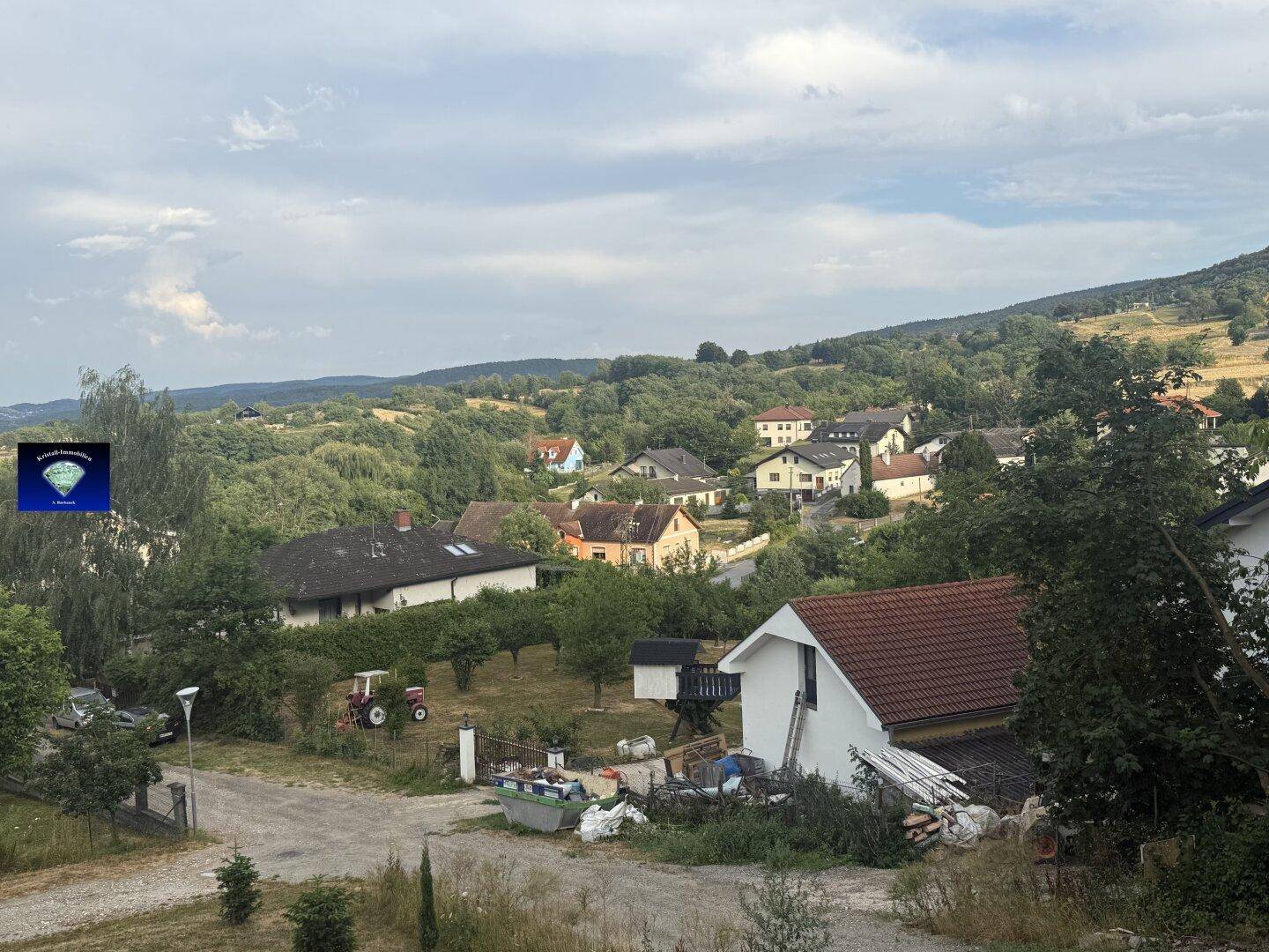 Panoramablick auf ein malerisches Dorf in einer grünen Hügellandschaft mit verstreuten Häusern.