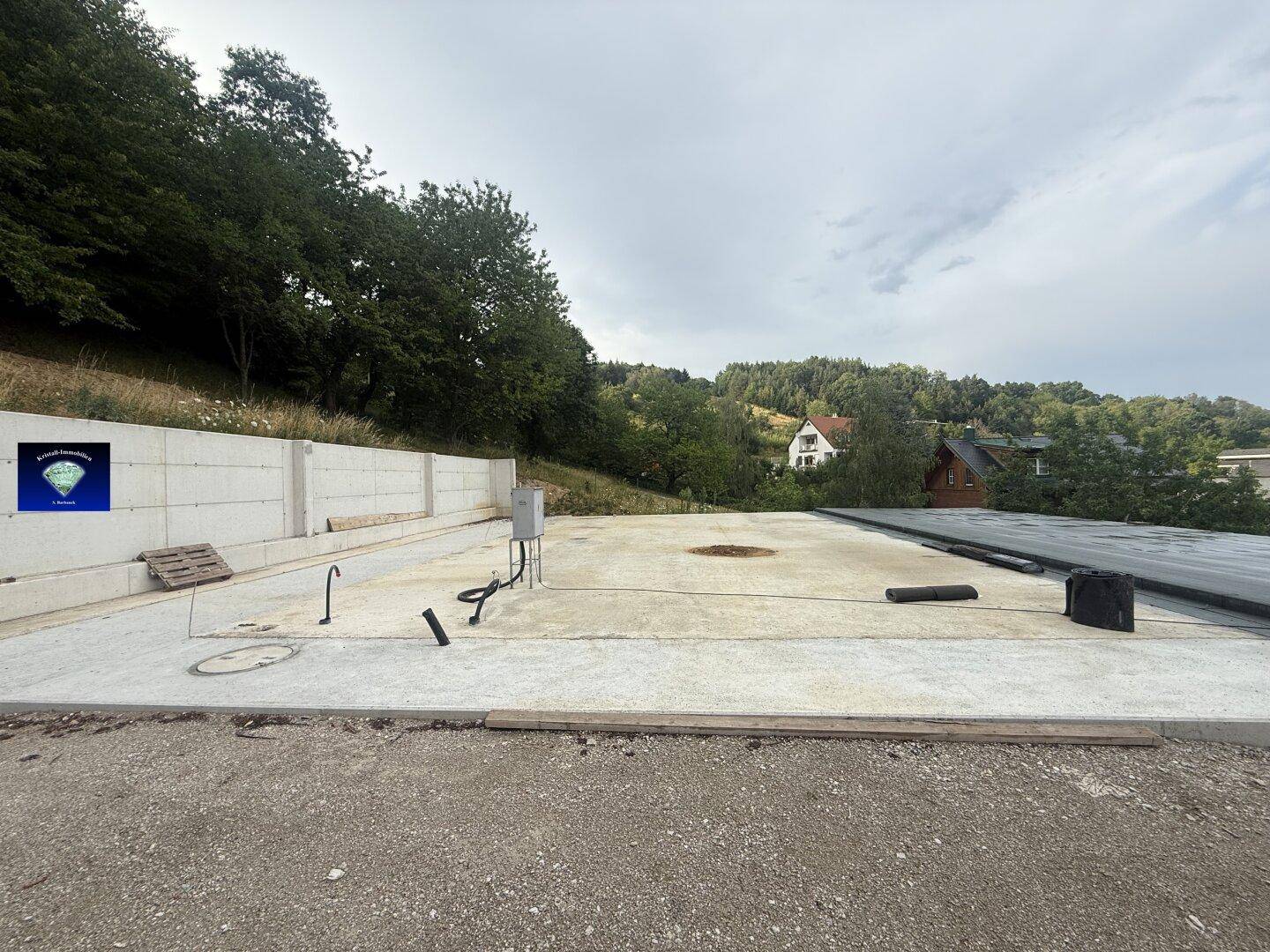 Baustelle mit vorbereiteter Betonplatte, Installationen und Blick auf Häuser in der Ferne.