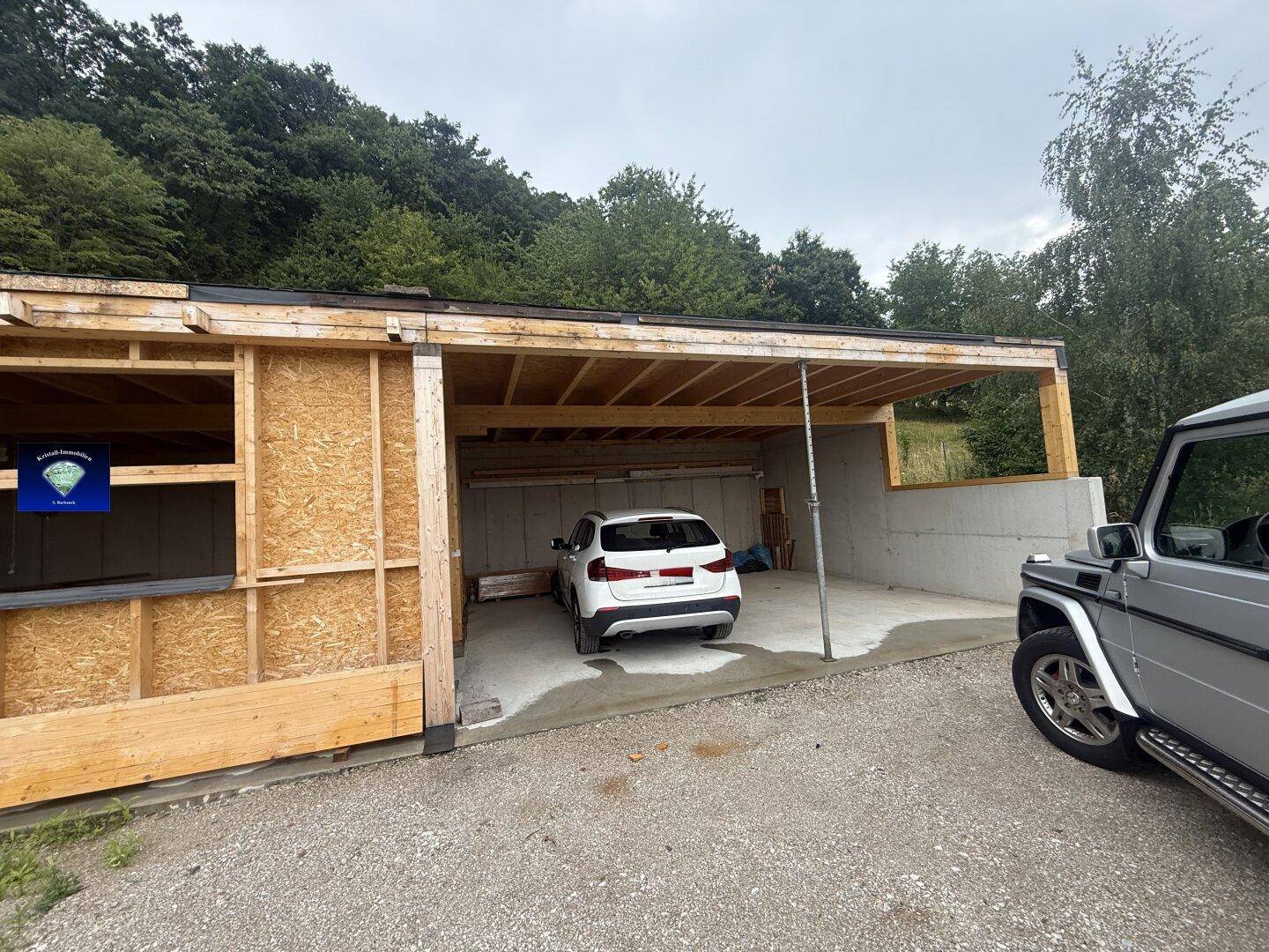 Außenansicht eines Hauses im Bau mit einem Carport, in dem ein Auto parkt, und Holzrahmenwänden.