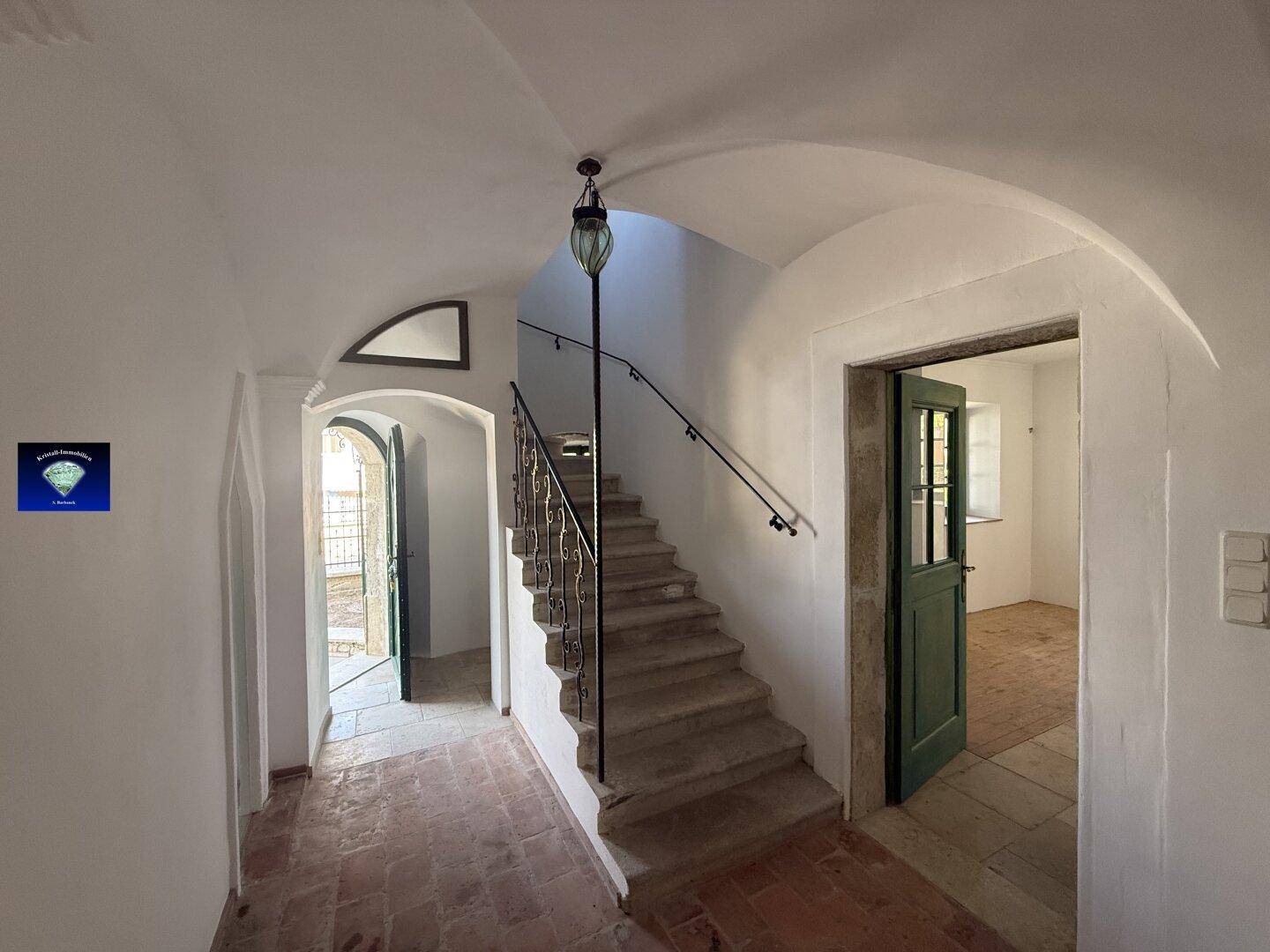 Historischer Flur mit Terrakottafliesen, Gewölbedecke und steinerner Treppe mit schmiedeeisernem Geländer.