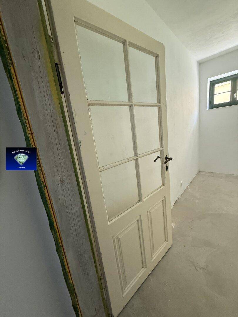 Weiße Holztür mit Glaseinsätzen lehnt in einem leeren Raum mit kleinem Fenster, bereit zur Installation.