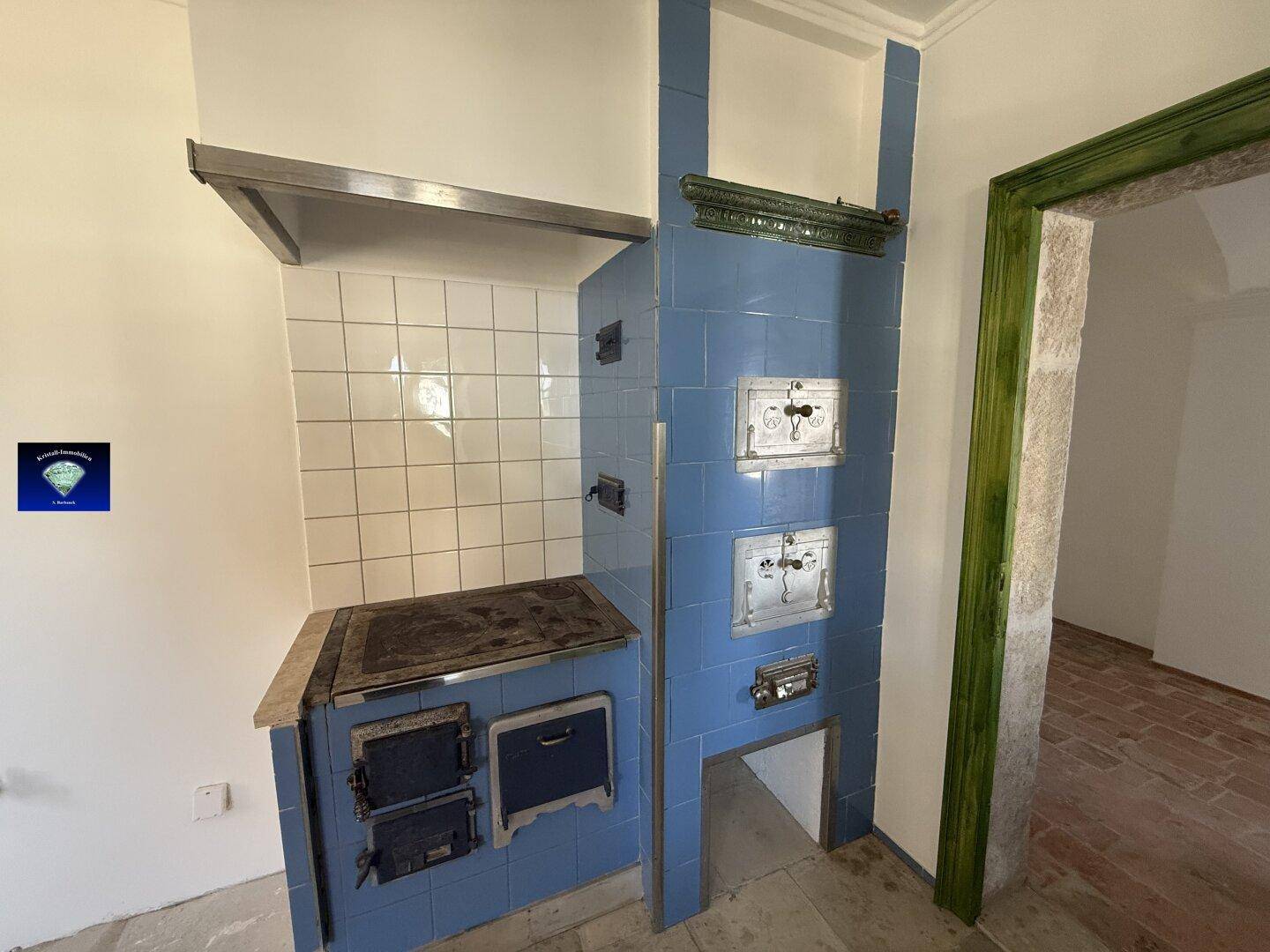 Traditionelle Küche mit blauem Kachelofen, weißem Fliesenspiegel und Dunstabzugshaube, rustikaler Charme.