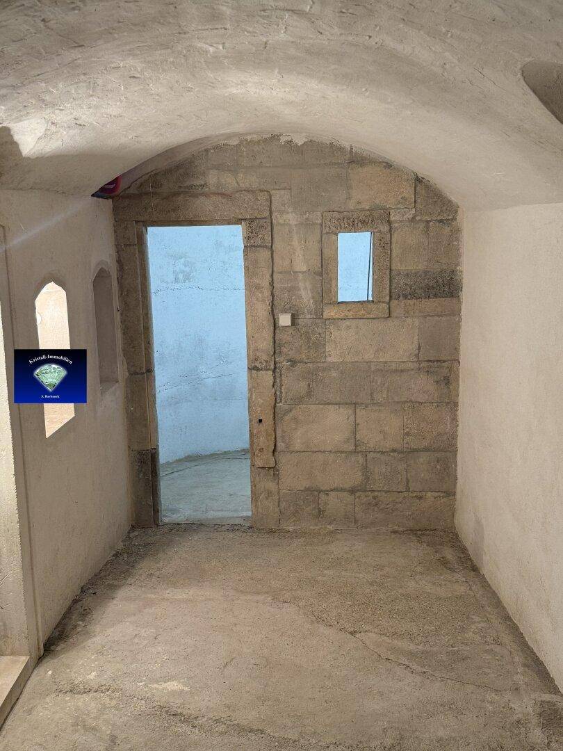 Rustikaler Kellerraum mit Steinmauern und Gewölbedecke, ein Durchgang führt in einen weiteren Bereich.