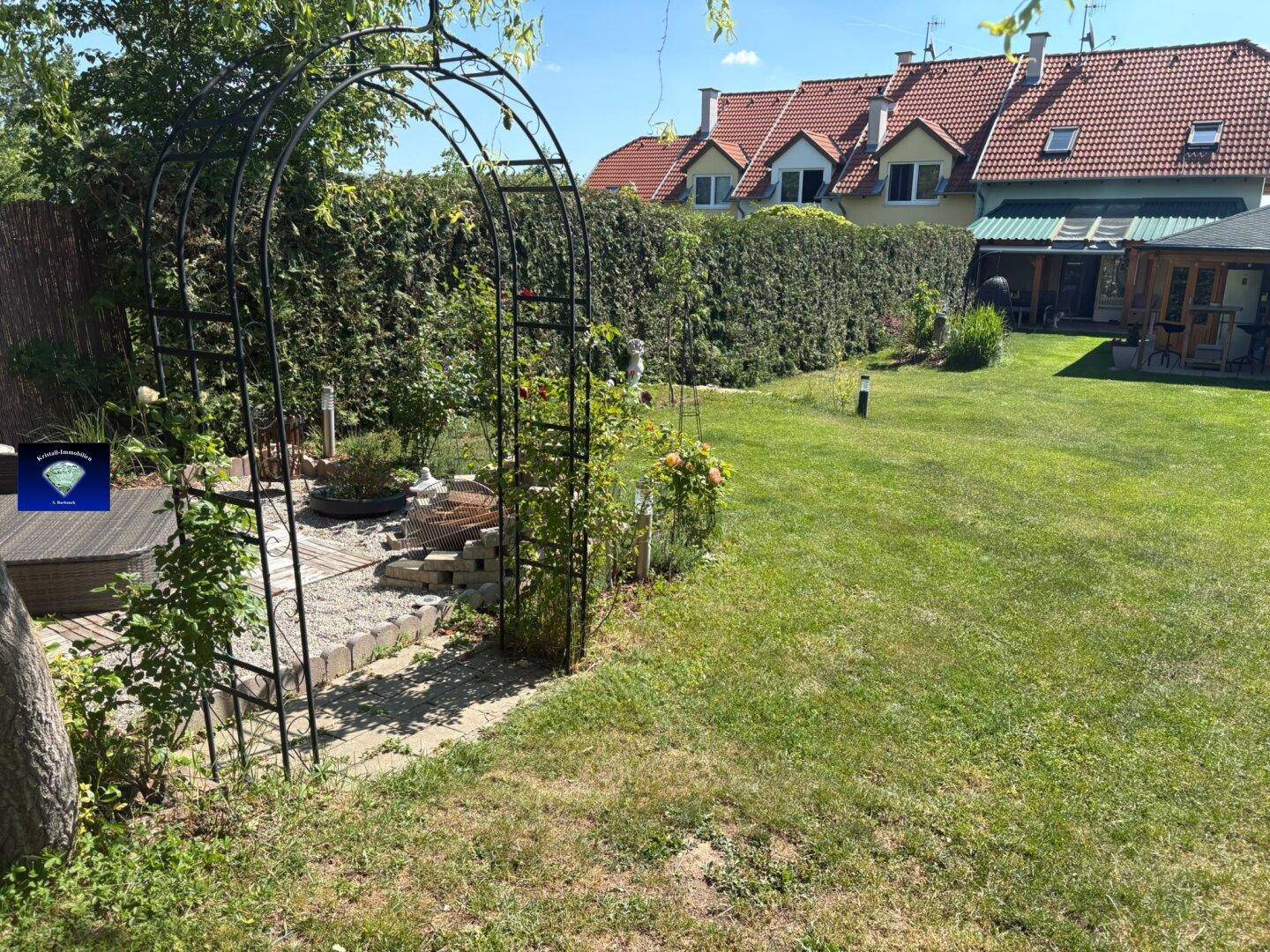 Gepflegter Garten mit großer Rasenfläche, hohen Hecken und einem dekorativen Metallbogen.