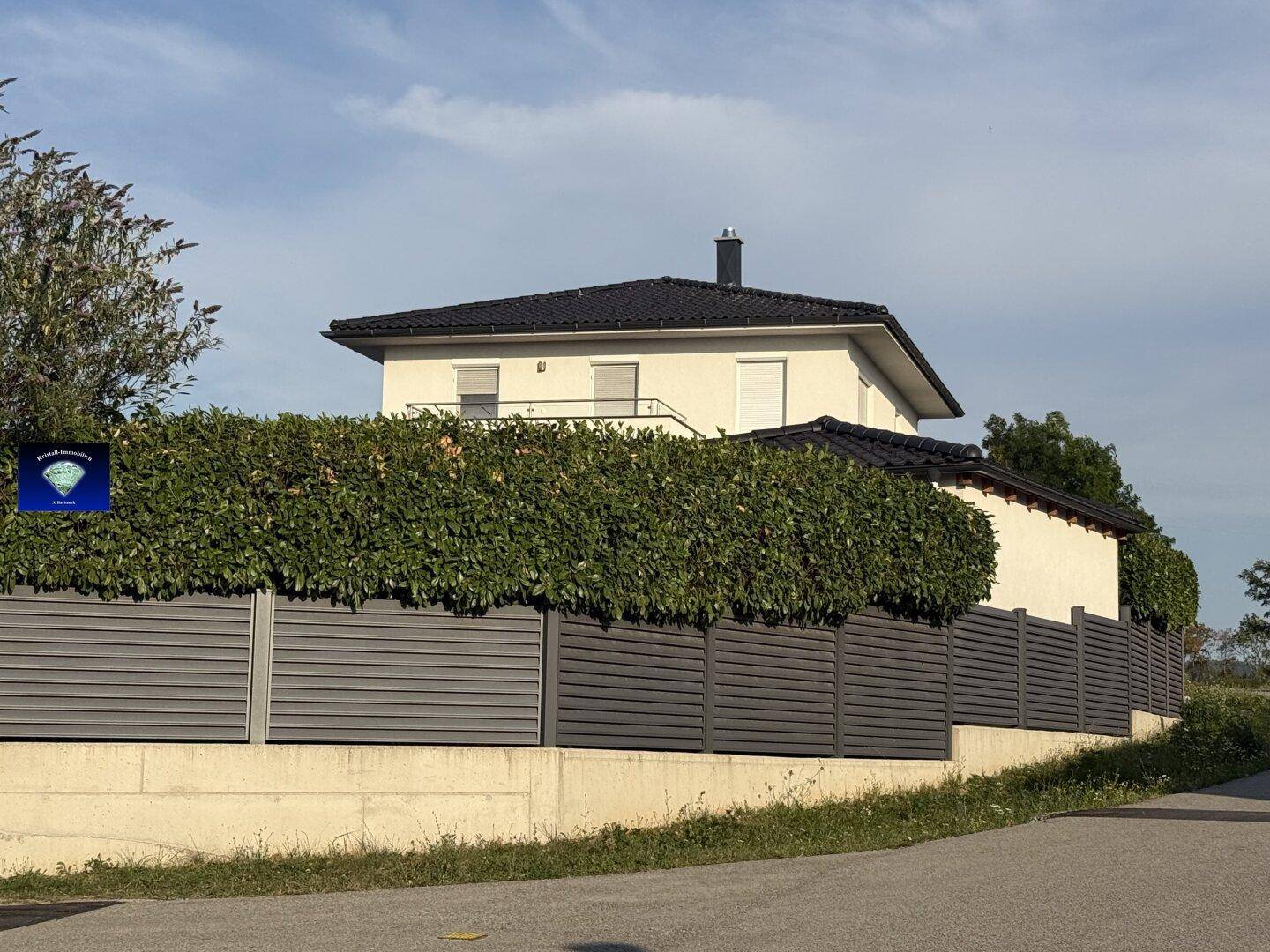 Modernes Einfamilienhaus mit gepflegter Hecke und Zaun, von der Straße aus gesehen.