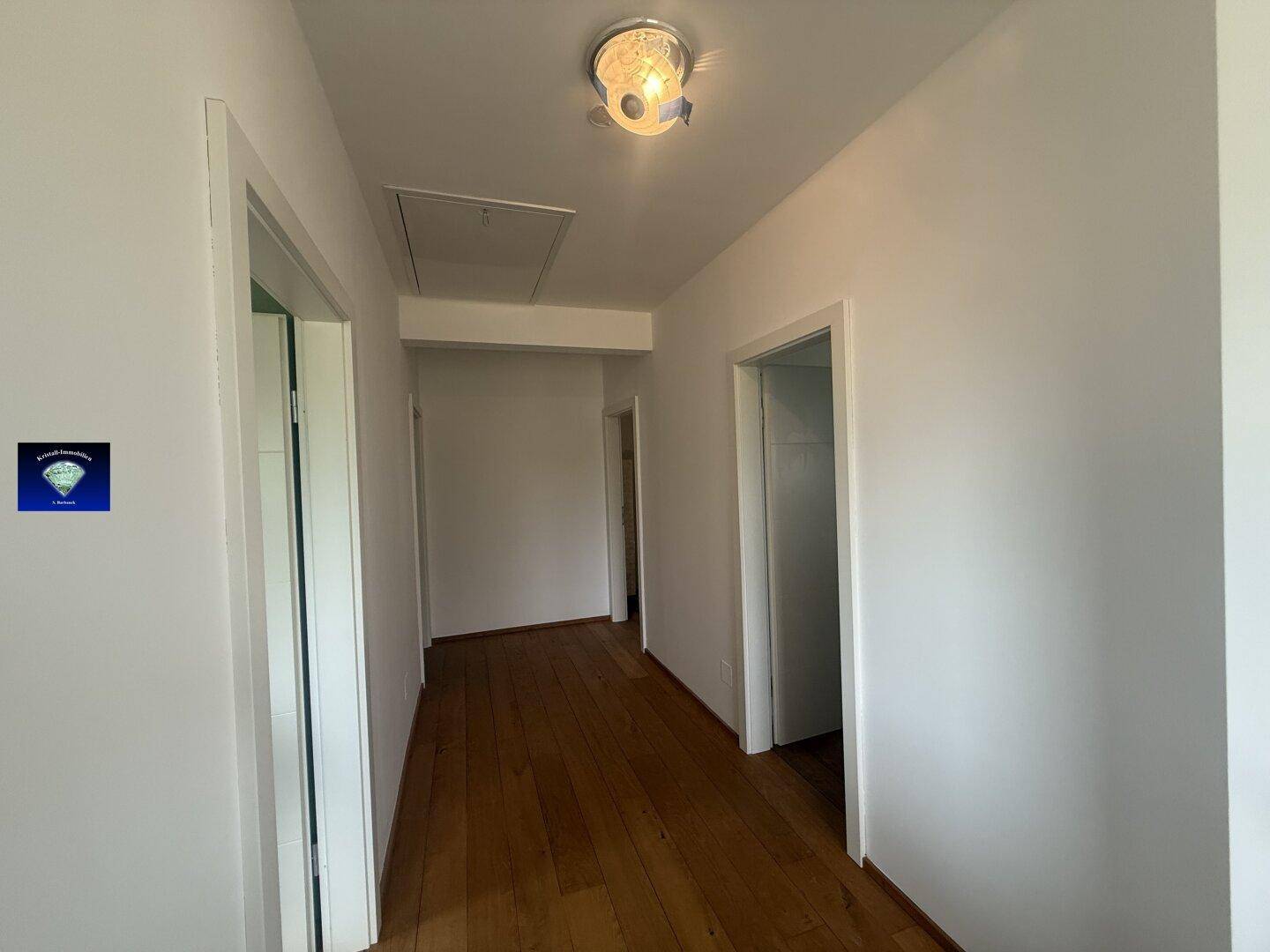 Heller Flur mit Holzboden und weißen Wänden, der zu weiteren Räumen führt.