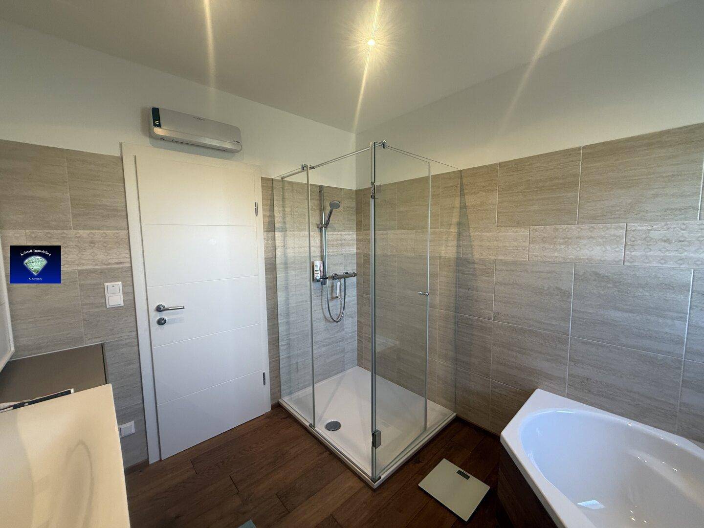 Modernes Badezimmer mit Duschkabine, Badewanne und Holzboden, hell gefliest.