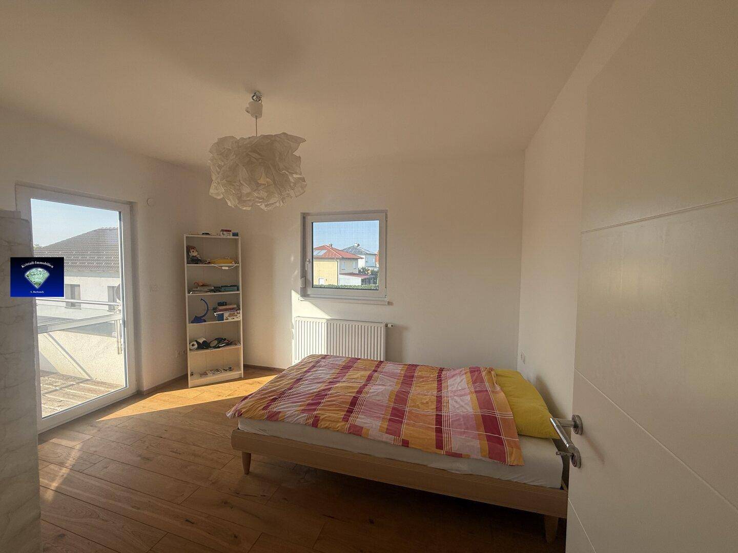 Helles Schlafzimmer mit Holzboden, Bett und Zugang zu einem Balkon oder einer Terrasse.