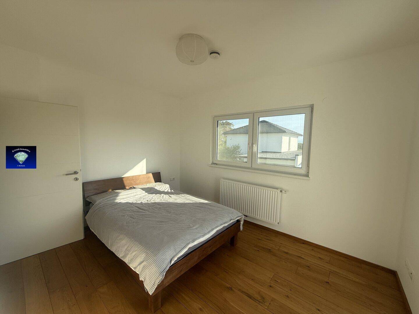Schlafzimmer mit Holzboden, Doppelbett und großem Fenster, das viel Licht hereinlässt.