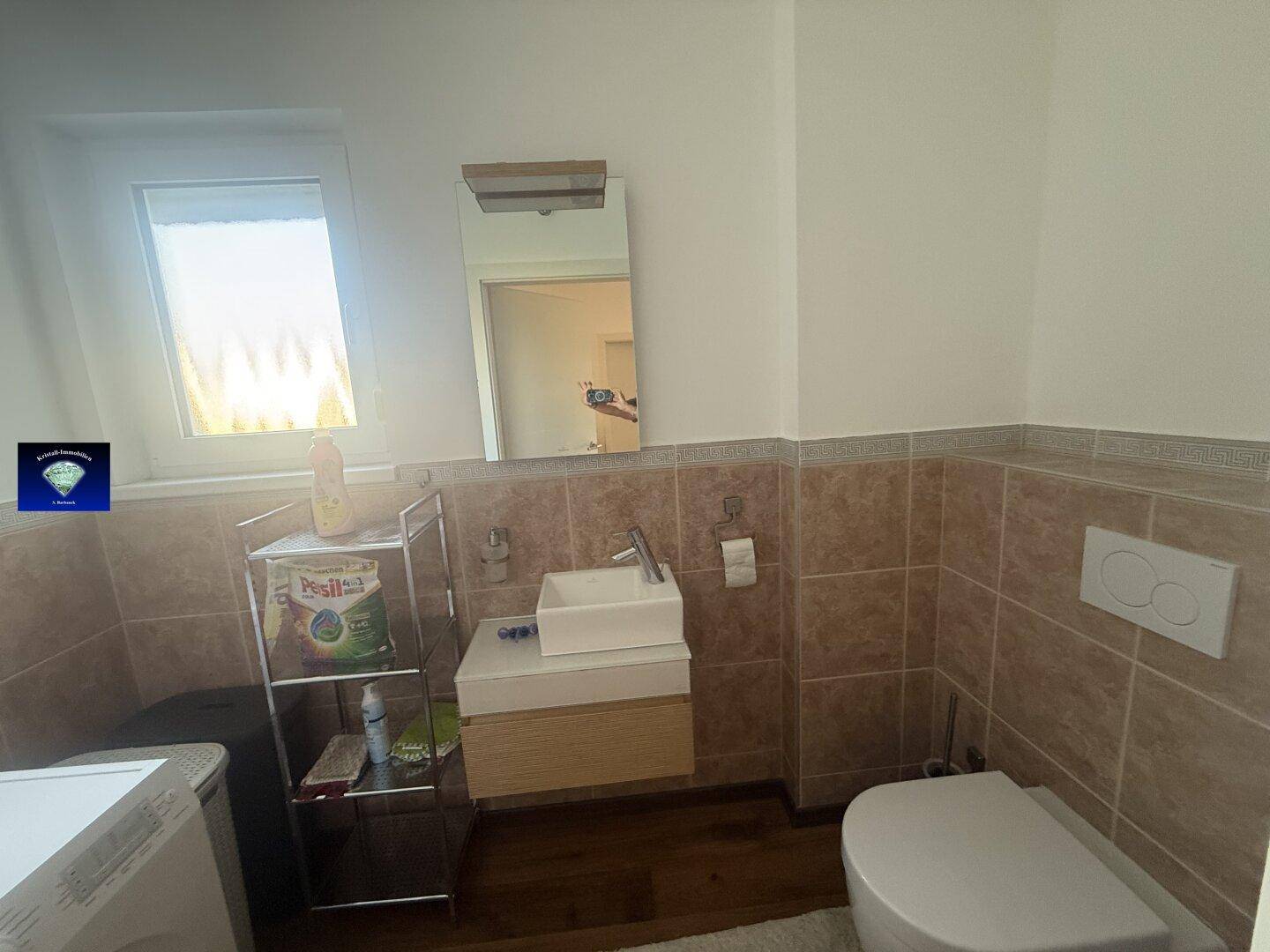 Kleines Gäste-WC mit Waschbecken, Toilette und Fenster, hell gefliest.