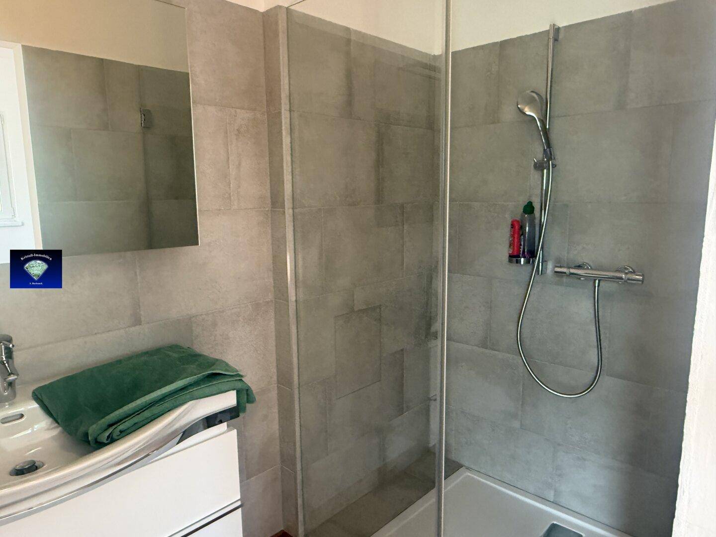 Modernes Badezimmer mit Duschkabine, Waschtisch und großem Spiegel, grau gefliest.