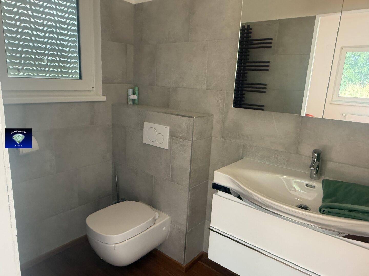 Modernes Badezimmer mit Waschtisch, Toilette und Spiegel, in Grautönen gehalten.