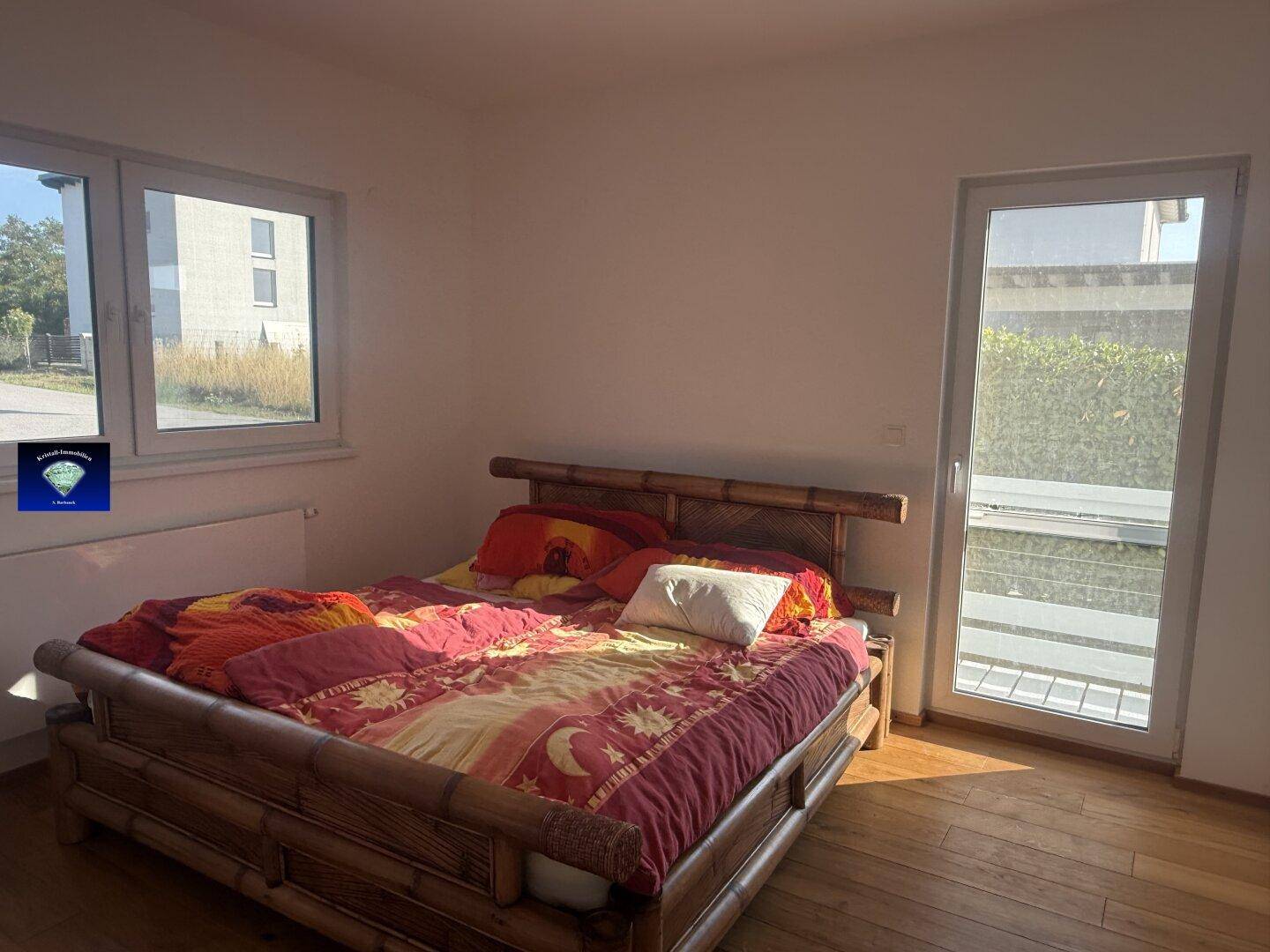 Helles Schlafzimmer mit Holzboden, Doppelbett und Zugang zu einem Außenbereich.