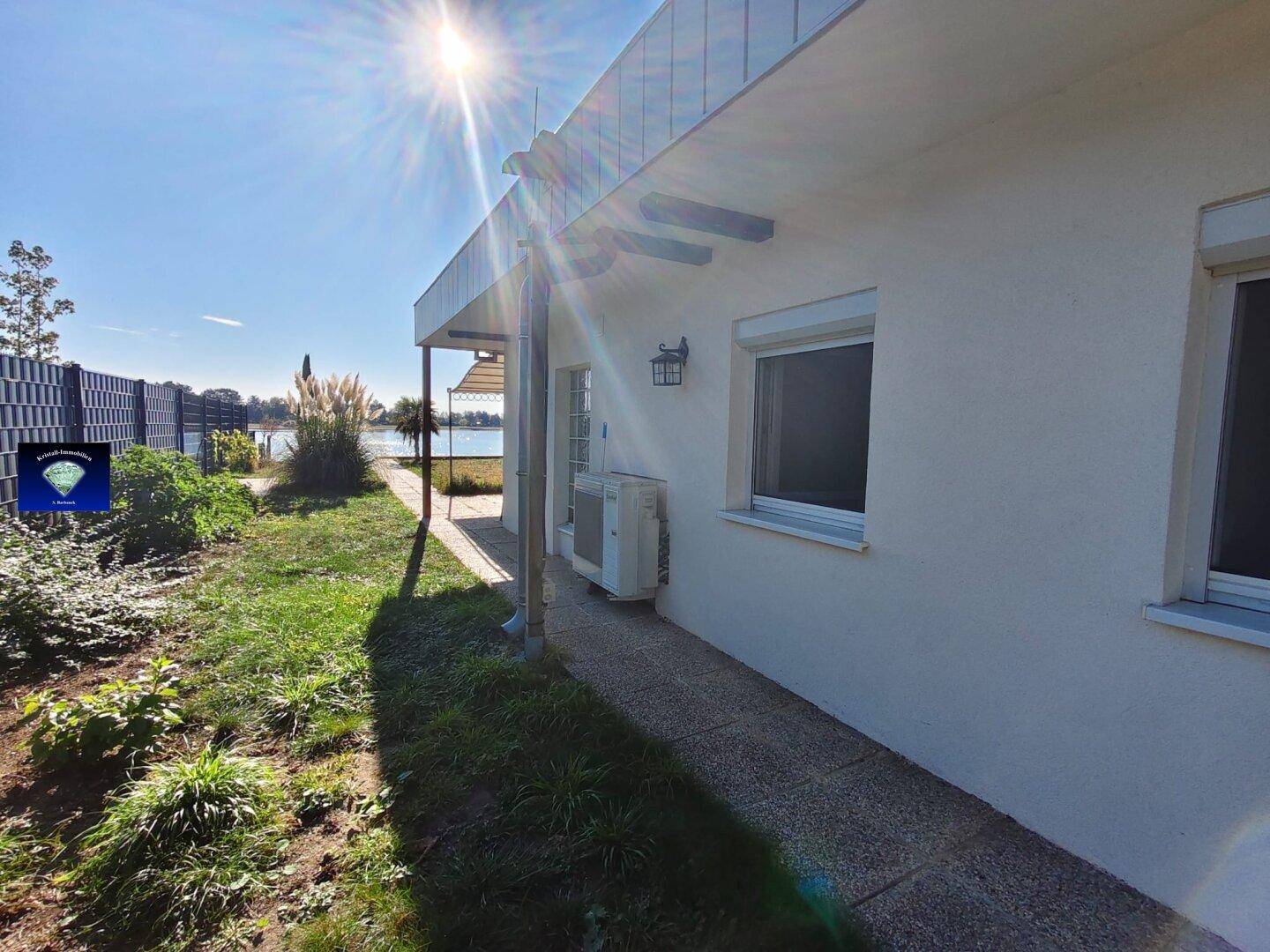 Seitenansicht des Hauses mit Garten, Weg und Klimaanlage, mit Seeblick im Hintergrund.