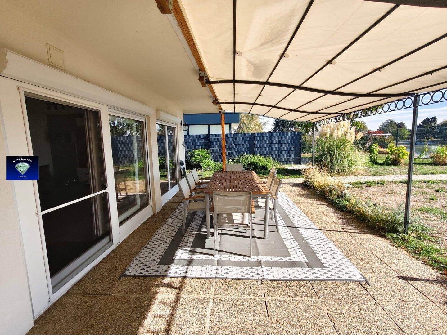 Überdachte Terrasse mit Esstisch und Stühlen, großen Glasschiebetüren und Seeblick.