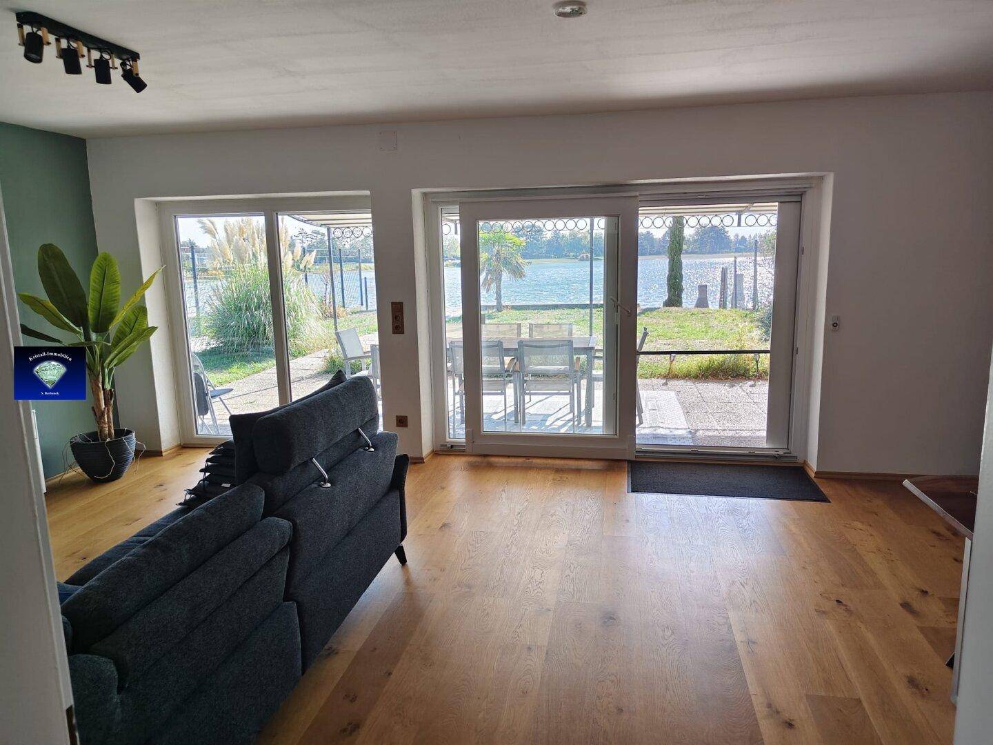 Helles Wohnzimmer mit Holzboden und großen Schiebetüren, die zur Terrasse und zum See führen.