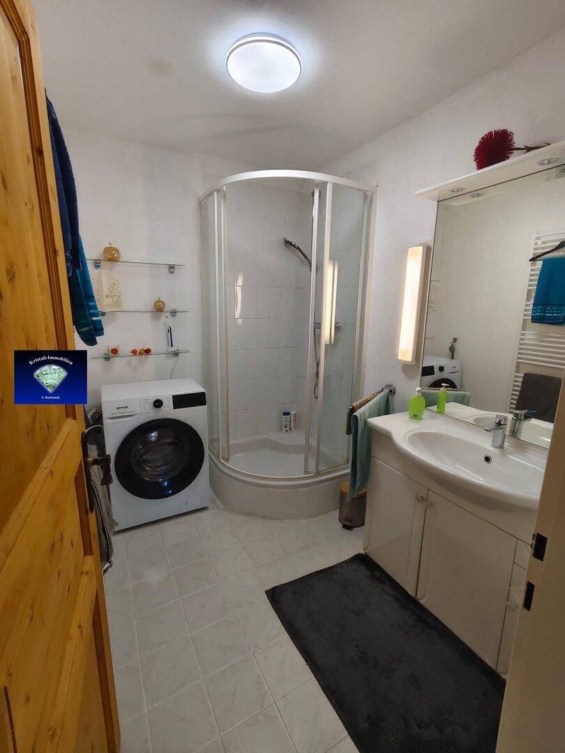 Badezimmer mit Eckdusche, Waschbecken, Waschmaschine und beheiztem Handtuchhalter.