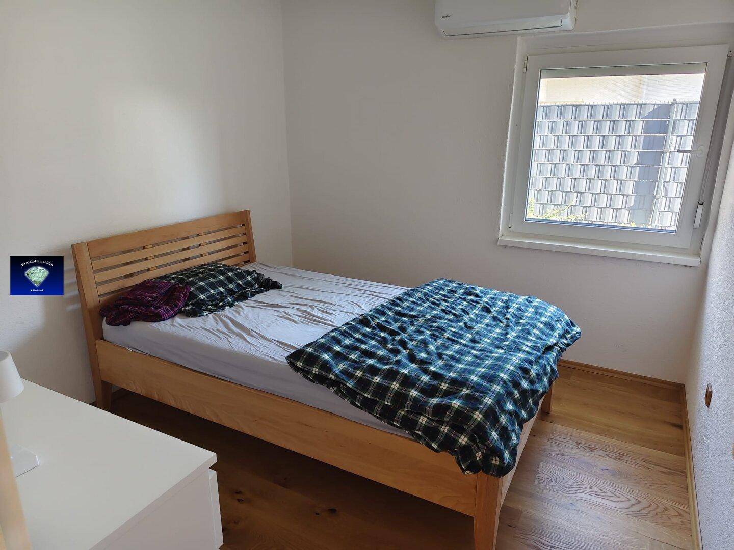 Schlafzimmer mit Holzbett, Fenster mit Rollladen, Holzboden und Klimaanlage.