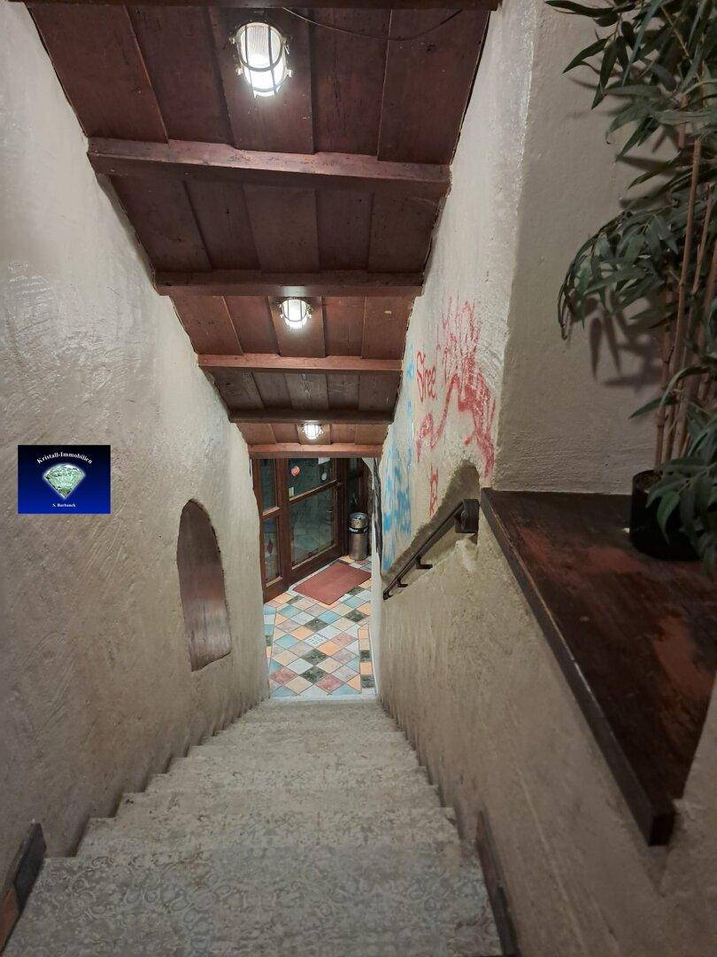 Rustikale Treppe mit rauen, hellen Wänden und einer Holzbalkendecke, die nach unten führt.