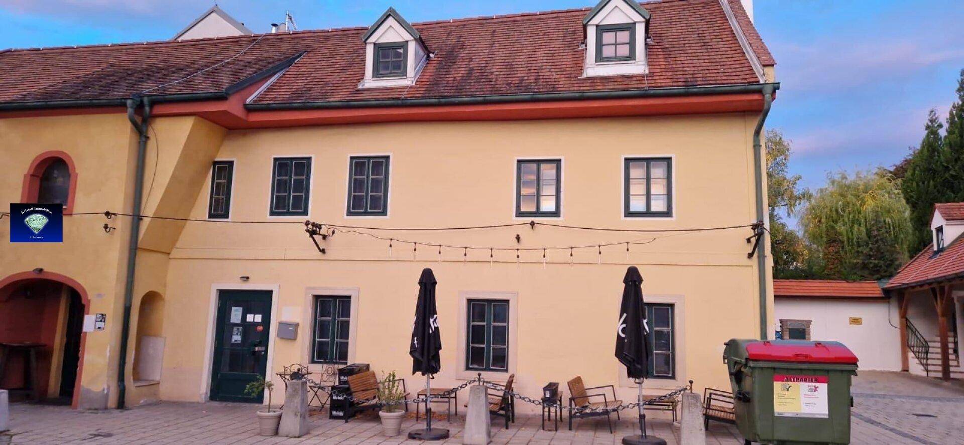 Rückseite eines traditionellen gelben Gebäudes mit roten Ziegeldächern und mehreren Fenstern.