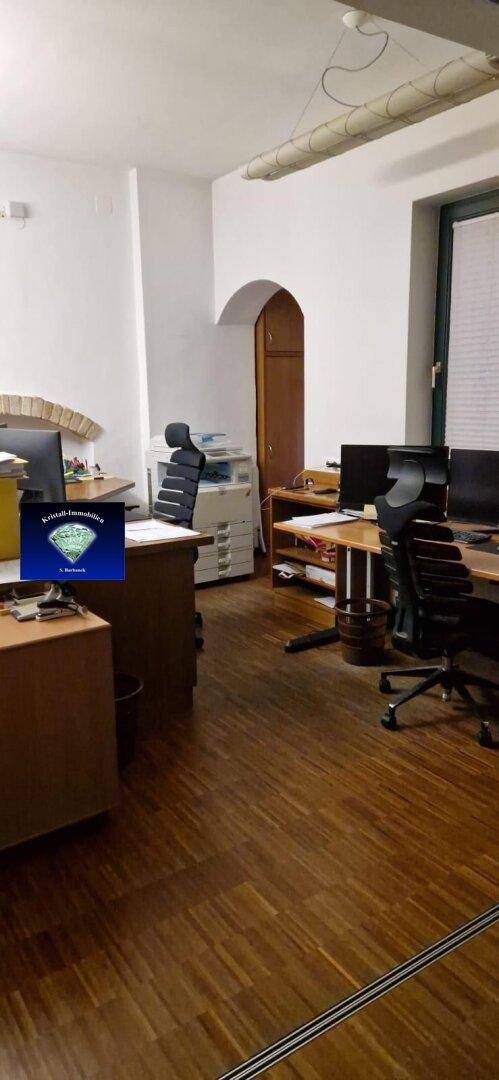 Helles Büro mit Holzboden, mehreren Arbeitsplätzen und einem modernen Drucker.