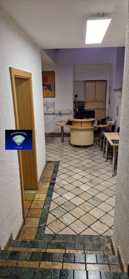 Flur mit gemustertem Fliesenboden, der zu einem offenen Bürobereich führt.