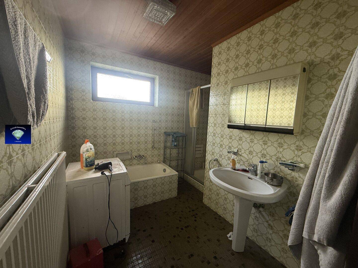 Badezimmer im Stil der 80er Jahre mit Badewanne, Waschbecken und gemusterten Fliesen.
