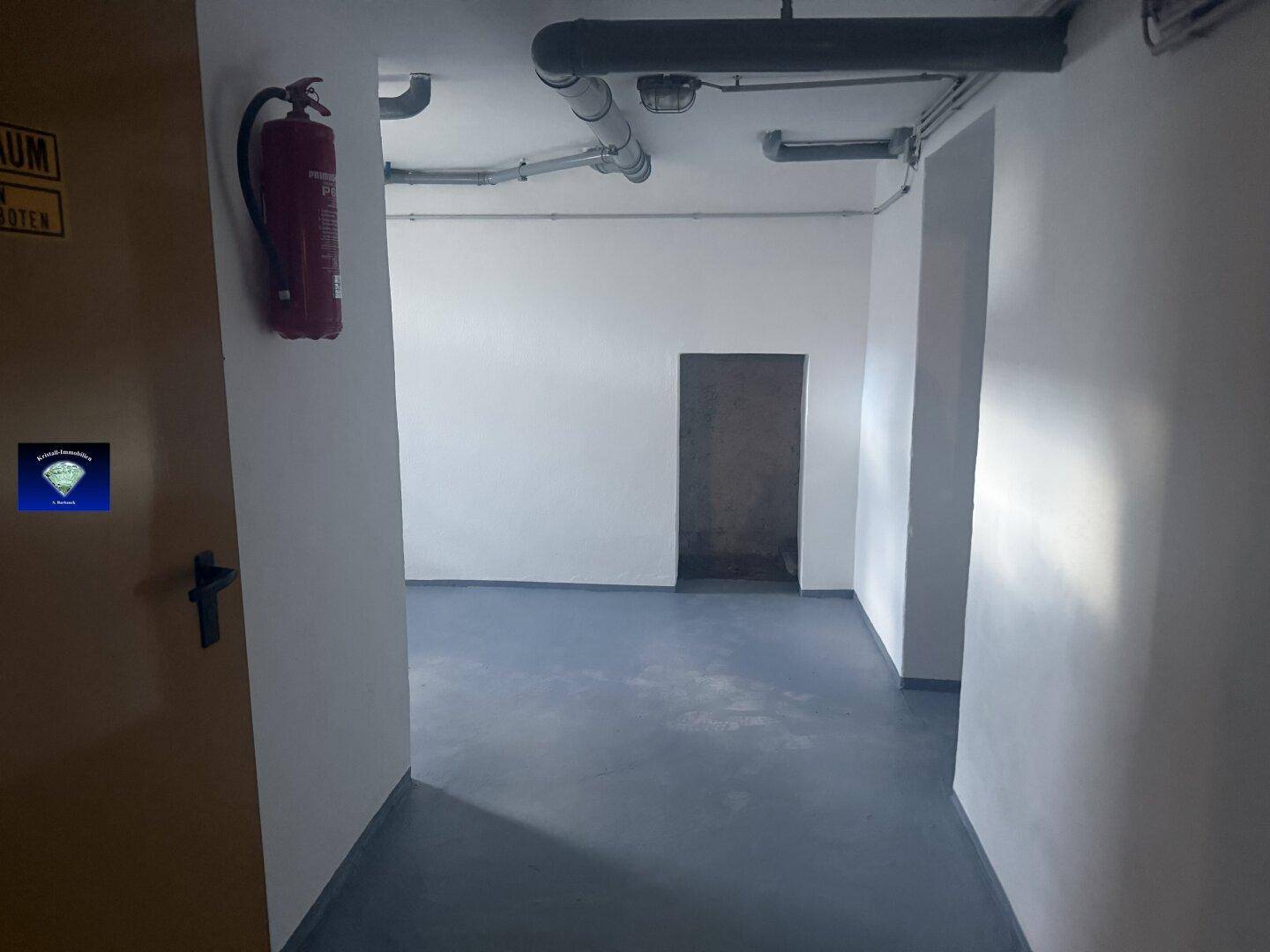 Langer Kellerflur mit weiß gestrichenen Wänden und einem Feuerlöscher an der Wand.