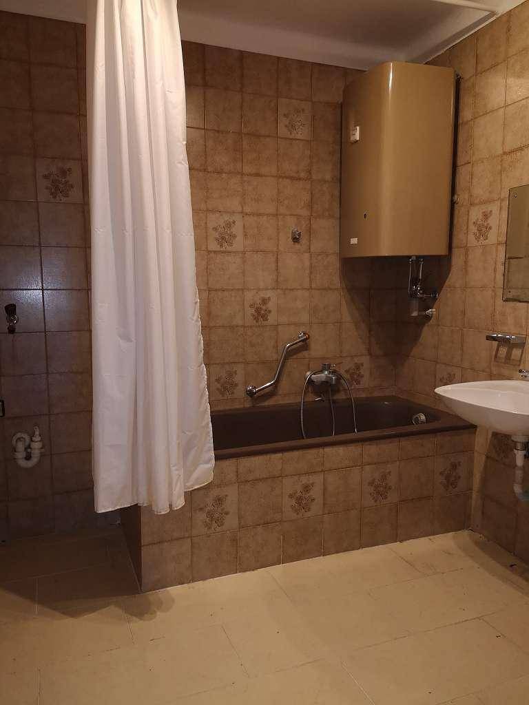Badezimmer mit braunen Fliesen, einer Badewanne mit Duschvorhang und einem Wandboiler.